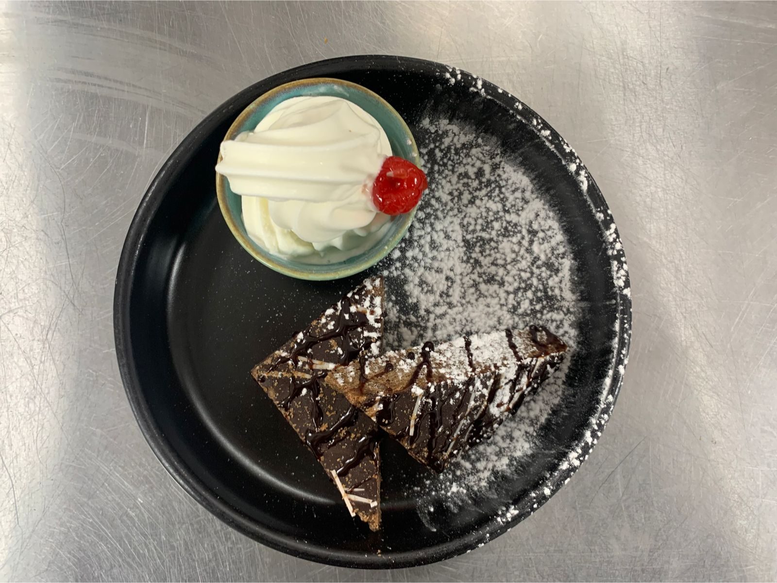 Chocolate brownie dessert with chantilly cream and a cherry, dusted with icing sugar