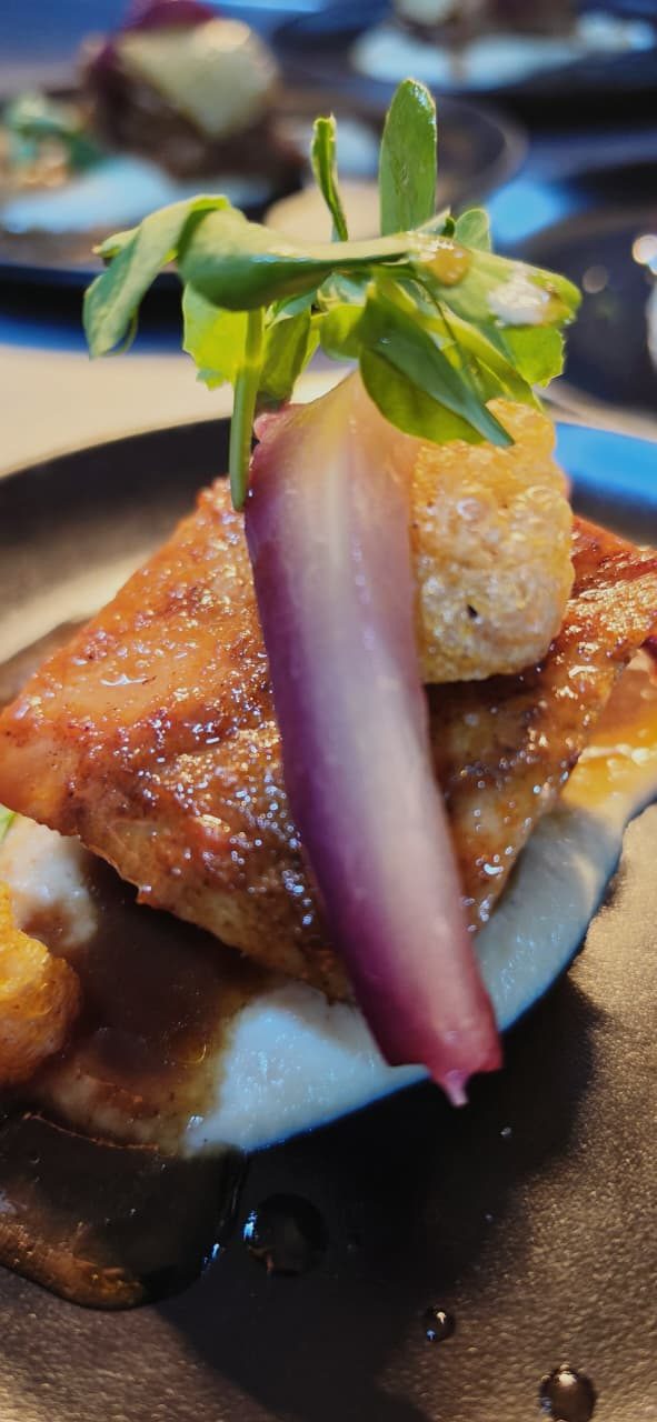 Crispy pork belly with crackling, red-wine pear and pea shoots on cauliflower purée