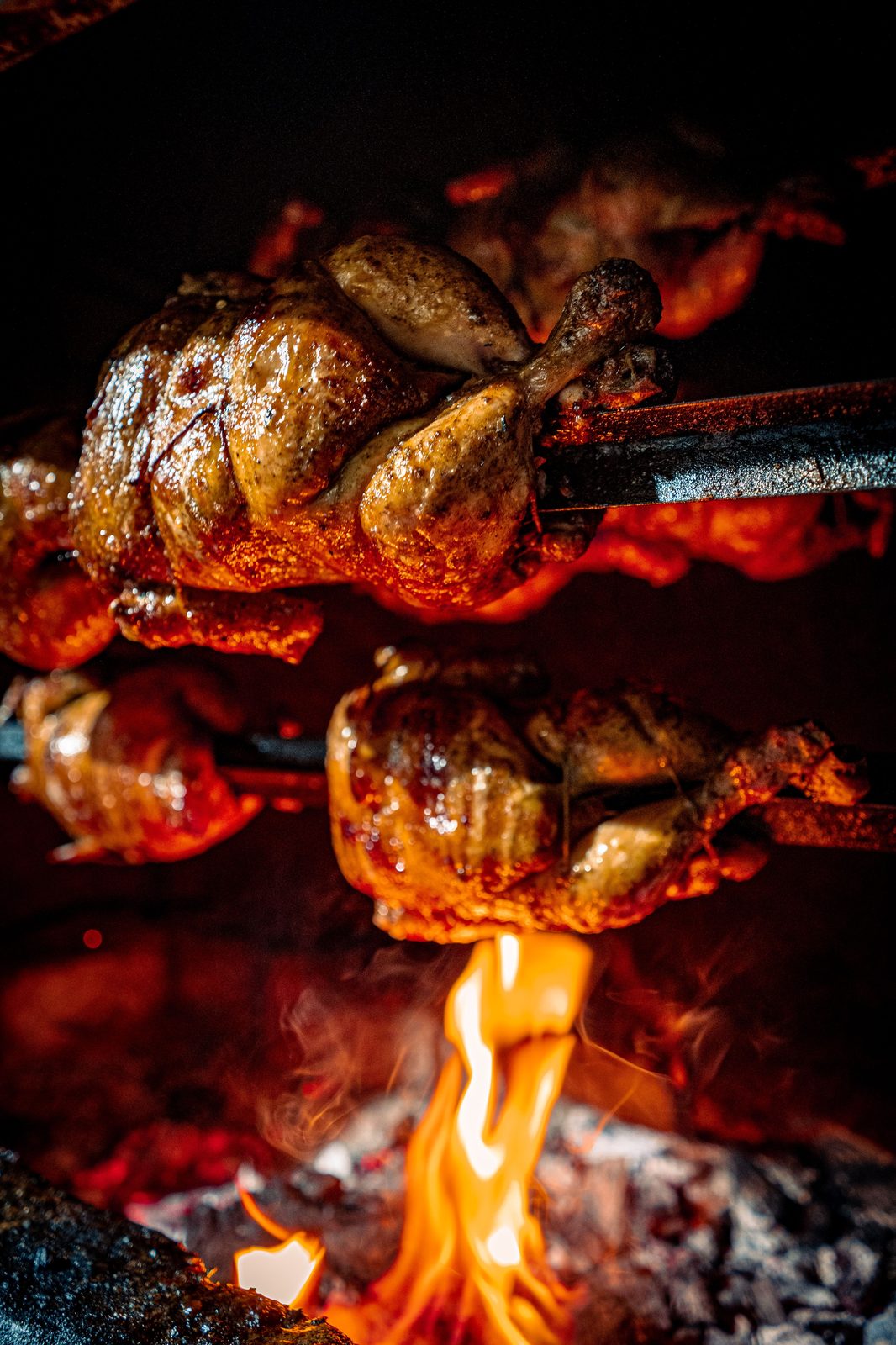 Whole chickens roasting on spits over open flames